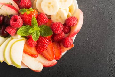 Çilek, elma, kiraz, muz ve kopya alanı siyah zemin üzerine beyaz tabakta ahududu meyve plaka