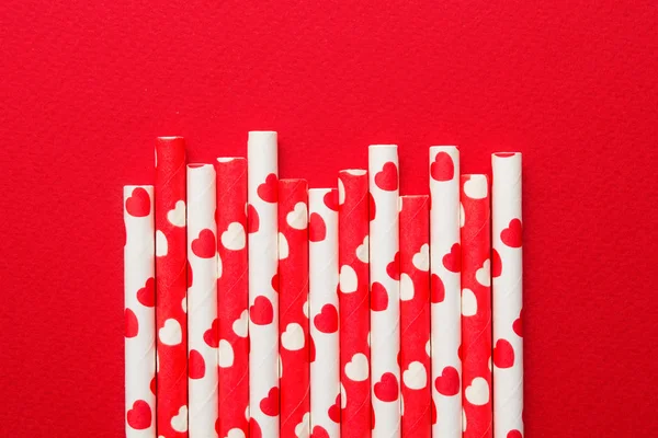 Red and white paper straw with hearts on red background, flat lay