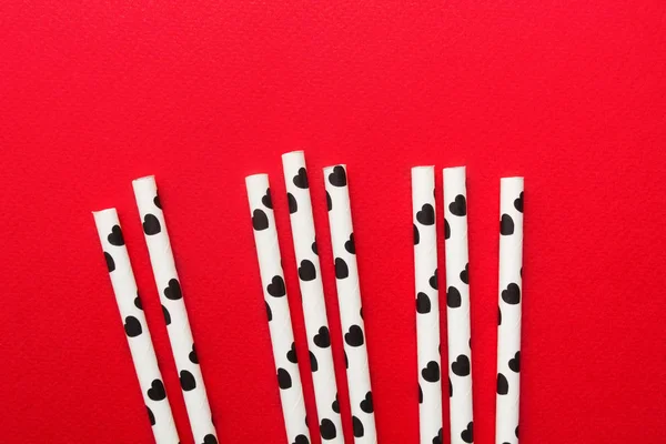 White paper straw with black hearts over red background, flat lay