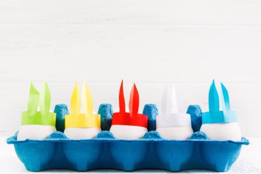 Kağıt renkli el yapımı tavşan kulaklı kopya alanı beyaz zemin üzerine kağıt mavi kapta beyaz Paskalya yumurtaları