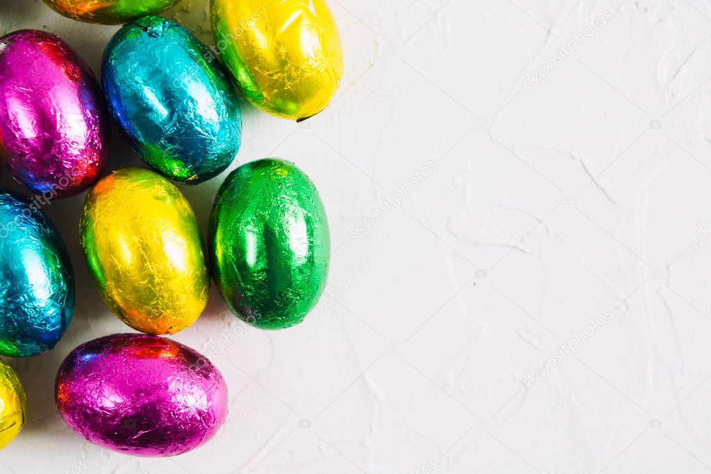 Easter background with colorful chocolate sweet eggs on white textured background