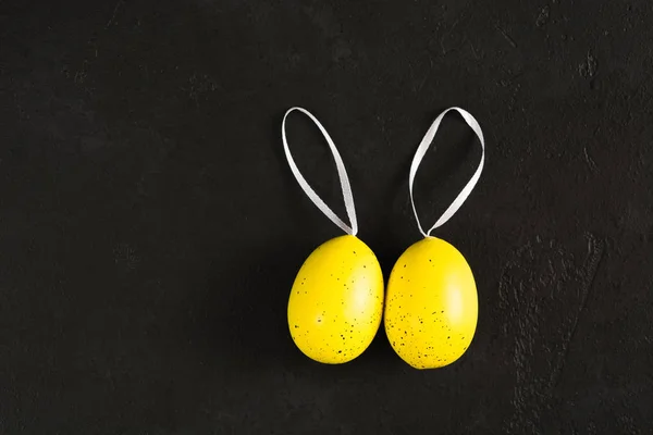 Deux œufs de couleur jaune avec des points avec des rubans sur fond de béton texturé noir — Photo