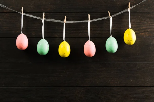 Huevos irreales coloridos de Pascua en la cuerda con fondo de madera. Foto oscura con espacio de copia — Foto de Stock