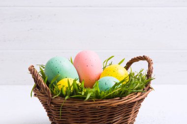 Beyaz ahşap arka plan ile sepet yeşil çim ile pastel renklerde Paskalya yumurtaları