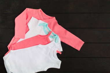 Kopya alanı ile kahverengi ahşap arka plan üzerinde pembe ve beyaz babysuits. Düz döşeme stili