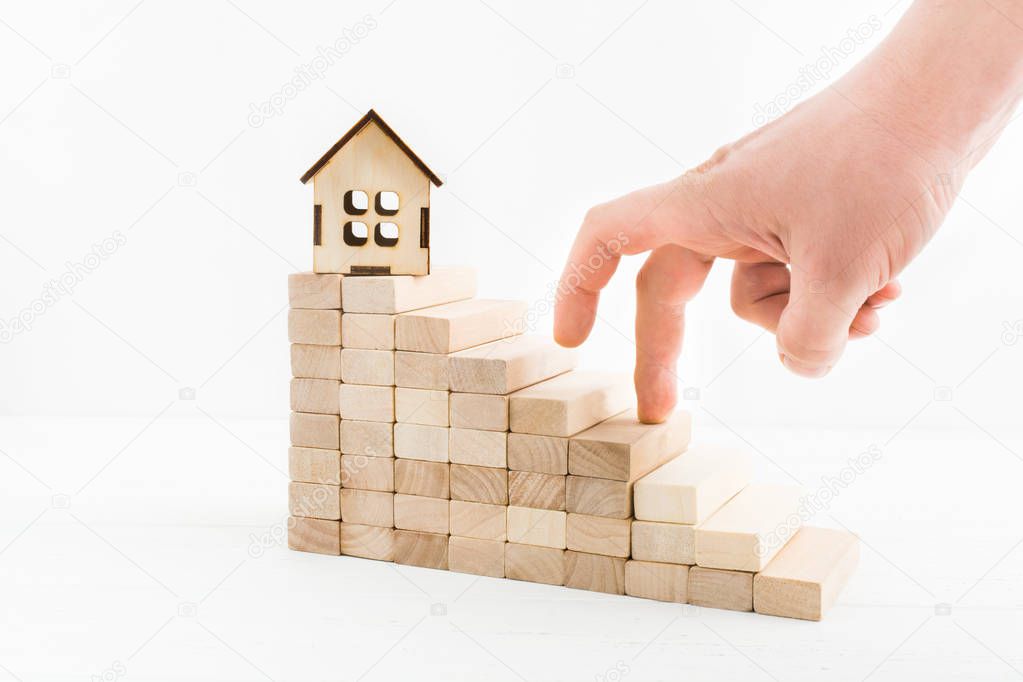 Wooden stairs of blocks with wooden house and man hand going up to stairs.