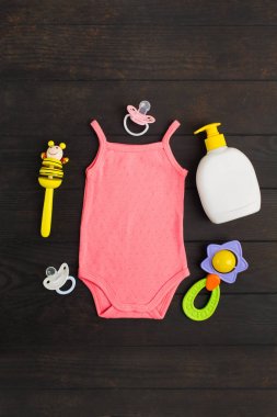Bebek duş aksesuarları. Pembe yaz bodysuit, iki sylicone emzik ve iki ahşap ve plastik çıngıraklı ahşap arka plan kopyalama alanı ile