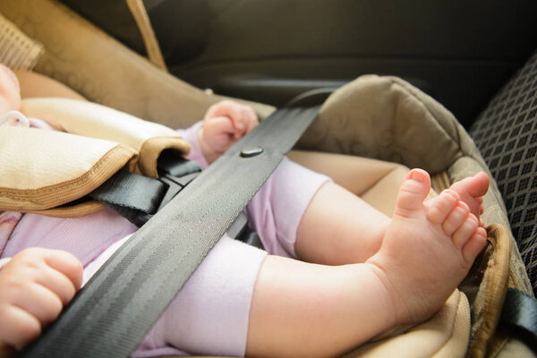 Safety concept, protection of child in travel, children feet in baby seat. Small baby sitting in special car seat with safety seatbelts