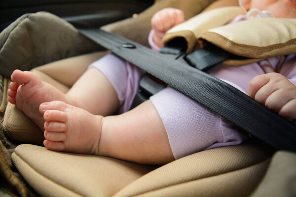 Концепция безопасности, защита ребенка в путешествии, детские ноги в детском кресле. Маленький ребенок сидит в специальном автомобильном кресле с ремнями безопасности
