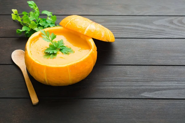 Kürbiscremesuppe in natürlicher Kürbisschale mit Petersiliendekoration und Holzlöffel über Holztisch mit Kopierraum — Stockfoto