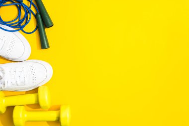 Beyaz spor ayakkabılar, dambıllar ve sarı arka planda ip atlama. Düz yatıyordu. Fitness ve sağlıklı yaşam tarzı konsepti. Boşluğu kopyala