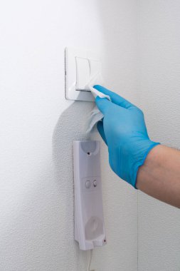 Mavi eldivenli bir adam kapıyı dezenfektanla temizliyor. Koronavirüs ve diğer virüslere karşı korunaklı. İnsan dokuya sıvı püskürtür.
