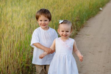 Küçük oğlan dikkatlice küçük kızların elini tutuyor. Uzağa bakıyorlar.