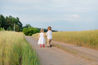 Küçük oğlan dikkatlice küçük kızların elini tutuyor. Uzağa bakıyorlar.