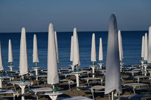 Katlanmış beyaz plaj şemsiyeleri ve deniz.