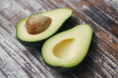 Ahşap masa üzerinde avokado bölünmüş kesim. Meyvenin iki yarısı. Biri çukurlu, diğeri de çukursuz. Vintage kesme tahtası.