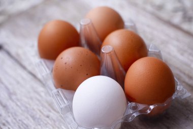 Ahşap masada altı yumurta plastik ambalaj. Farklı bir yumurta rengi. Beş kahverengi ve bir beyaz. 