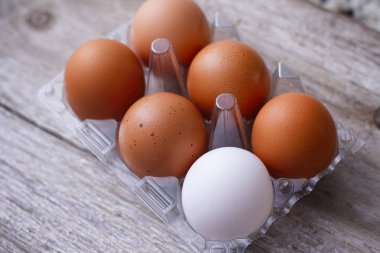 Ahşap masada altı yumurta plastik ambalaj. Farklı bir yumurta rengi. Beş kahverengi ve bir beyaz. 