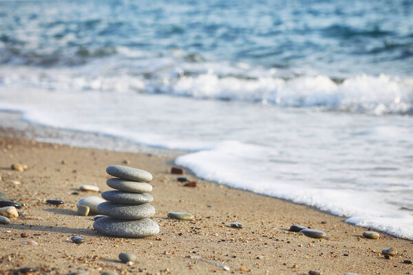 Дзен пирамида курортных камней на размытом морском фоне. Песок на пляже. Морские берега. Текстура волн воды. Левая сторона фотографии. Место для текста
. 