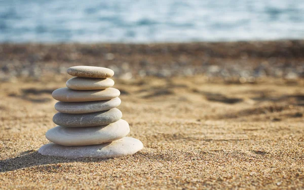 Zen pyramid of spa stones on the blurred sea background. Sand on a beach. Sea shores. Water waves texture. Left side of photo. Place for text.