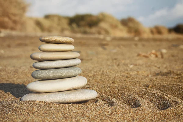 Zen pyramid of spa stones on the blurred sea background. Sand on a beach. Sea shores. Water waves texture. Left side of photo. Place for text.