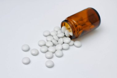 Sarı cam şişeden beyaz yuvarlak haplar. Beyaz arkaplanda. 