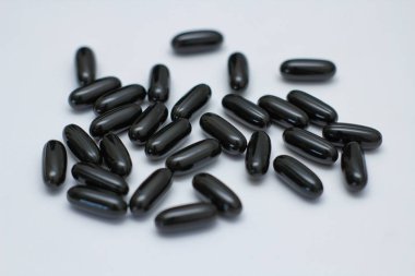 Beyaz arka planda birçok siyah oval hap. Sıvı ile kapsüller. Takviye -leri. 