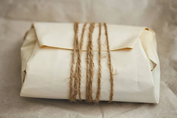 Paper wrapped parcel with hemp cord on brown background. Package for delivery.