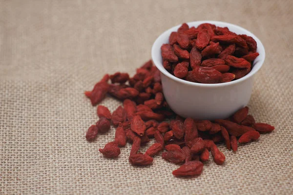 Dry goji berries on cloth texture background. Cup of dry fruits.