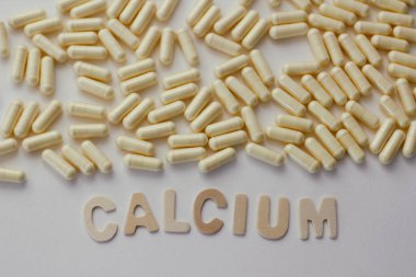 Kalsiyum takviyeleri kavramı. Beyaz arka planda beyaz ve sarı kapsül hapları. Ahşap harflerle metin.