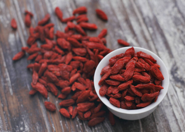 Dry goji berries in small white cup on wooden background. Super food concept. Dry fruits. 