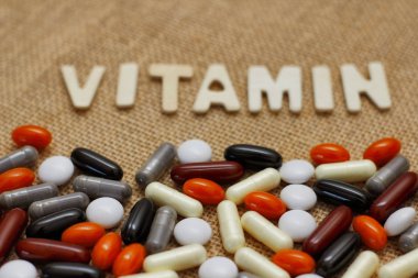 Kahverengi kaba kumaş doku üzerinde ahşap harflerle Vitamin kavram metni. Farklı haplar seti.