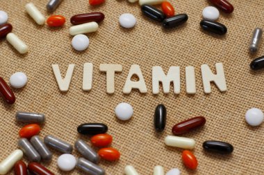 Kahverengi kaba kumaş doku üzerinde ahşap harflerle Vitamin kavram metni. Farklı haplar seti.