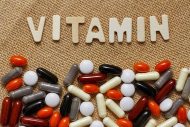 Kahverengi kaba kumaş doku üzerinde ahşap harflerle Vitamin kavram metni. Farklı haplar seti.