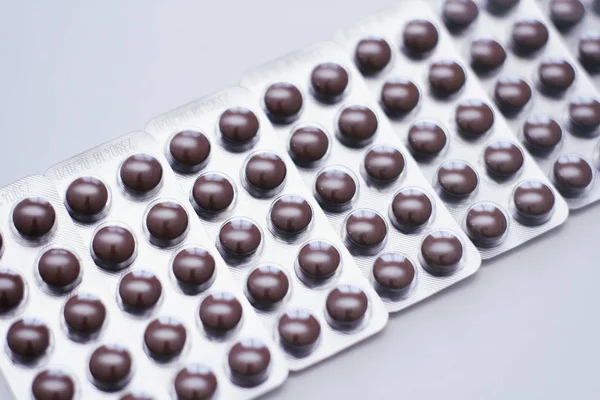 Brown round pills in clear plastic blisters on white background.
