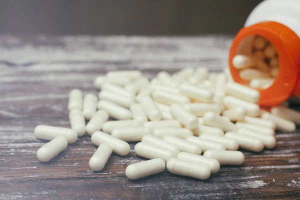 White capsules pills on old wooden table background. Medical concept.