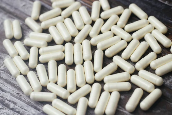 White capsules pills on old wooden table background. Medical concept.