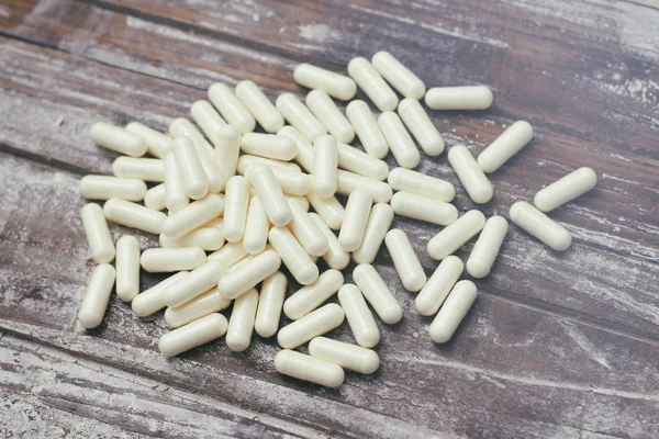 White capsules pills on old wooden table background. Medical concept.