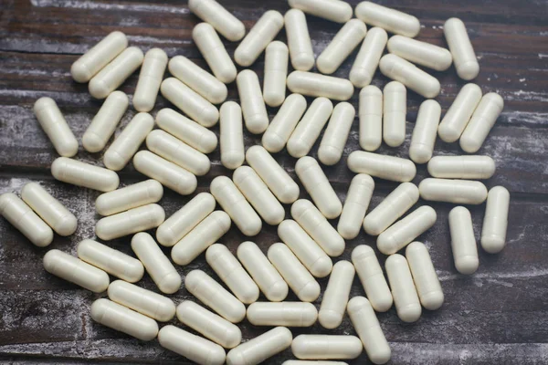 White capsules pills on old wooden table background. Medical concept.