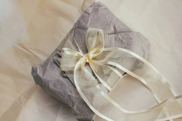 Soft parcel wrapped into old craft paper and tie. Crumpled background texture. Gift shop. Materials for transportation and shipping.