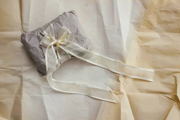 Soft parcel wrapped into old craft paper and tie. Crumpled background texture. Gift shop. Materials for transportation and shipping.