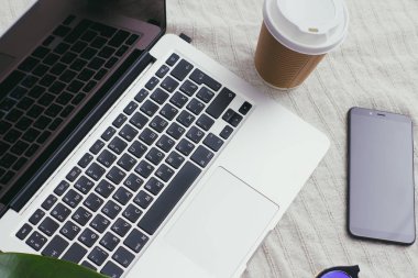 Dizüstü bilgisayarı, mavi güneş gözlüğü, cep telefonu, bir fincan kahve ve yeşil yapraklı bir iş yeri. Serbest meslek kavramı. Seyahat işindeyim. İnternetten alışveriş.