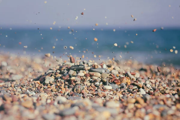 Kum ve küçük taşlar mavi deniz suyu arka plan üzerinde yere dökülen.