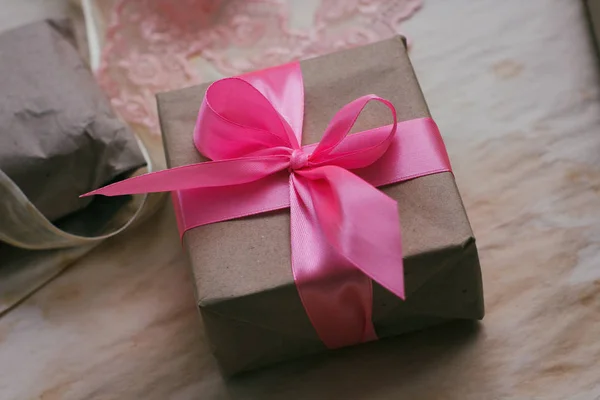 Gift box wrapped in brown craft paper and tied by pink satin ribbon. Packaging process. Gift shop. Wedding decor.