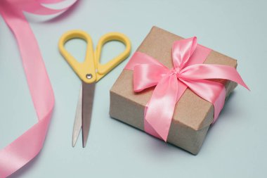 Hediyeler paketleme işlemi. Dekoratif kağıtlar, ipek kurdeleler, hediye kutuları, makaslar. Açık mavi arka plan. 