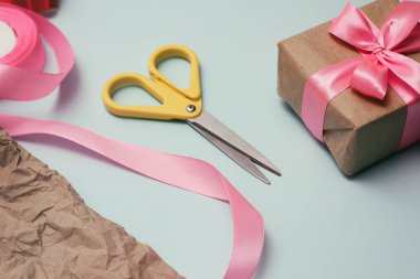 Hediyeler paketleme işlemi. Dekoratif kağıtlar, ipek kurdeleler, hediye kutuları, makaslar. Açık mavi arka plan. 