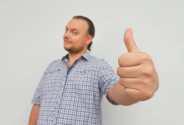 Damalı gömlekli genç adam başparmaklarını gösterir. Hipster serbest çalışan. 