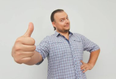 Damalı gömlekli genç adam başparmaklarını gösterir. Hipster serbest çalışan. 