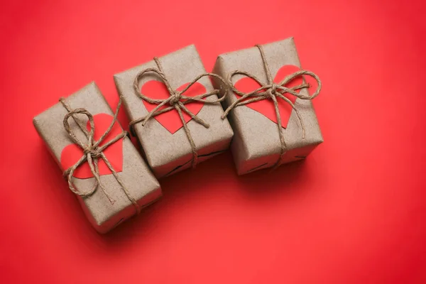 Romantic presents set. Gift boxes wrapped in brown craft paper and tie hemp string. Carton hearts. Red solid background. Delivered parcels.