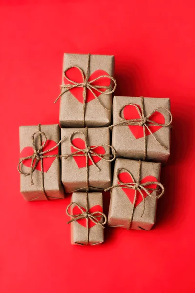 ロマンチックなプレゼントセット 茶色のクラフトペーパーとネクタイの麻の紐で包まれたギフトボックス カートンの心赤いソリッドの背景 配達された小包 — ストック写真